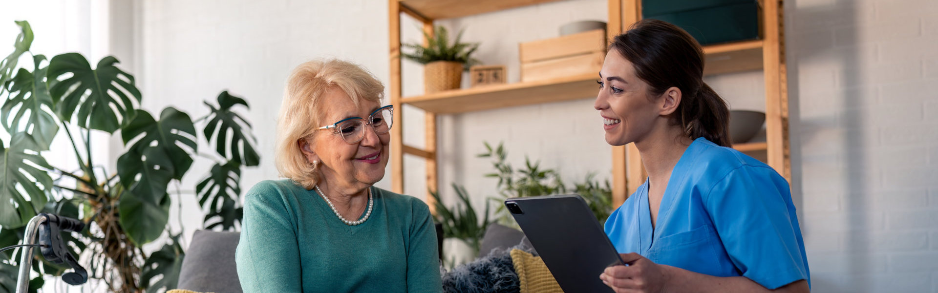 Smiling female home care worker using tablet and talking to senior woman patient